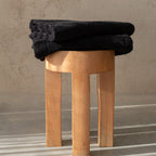 Stack of black towels on a wooden stool against a beige wall.