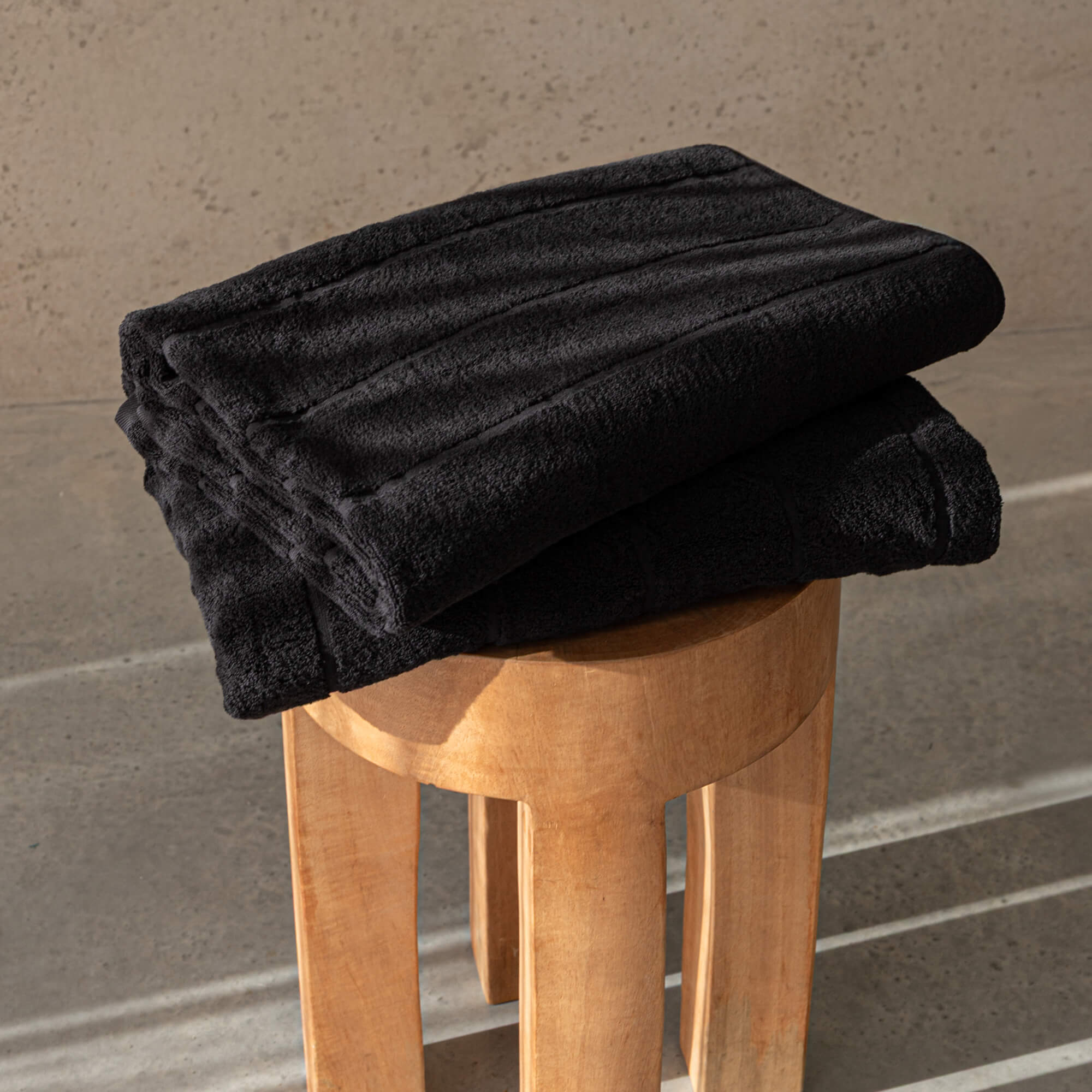 Folded black towel on a wooden stool against a beige wall.