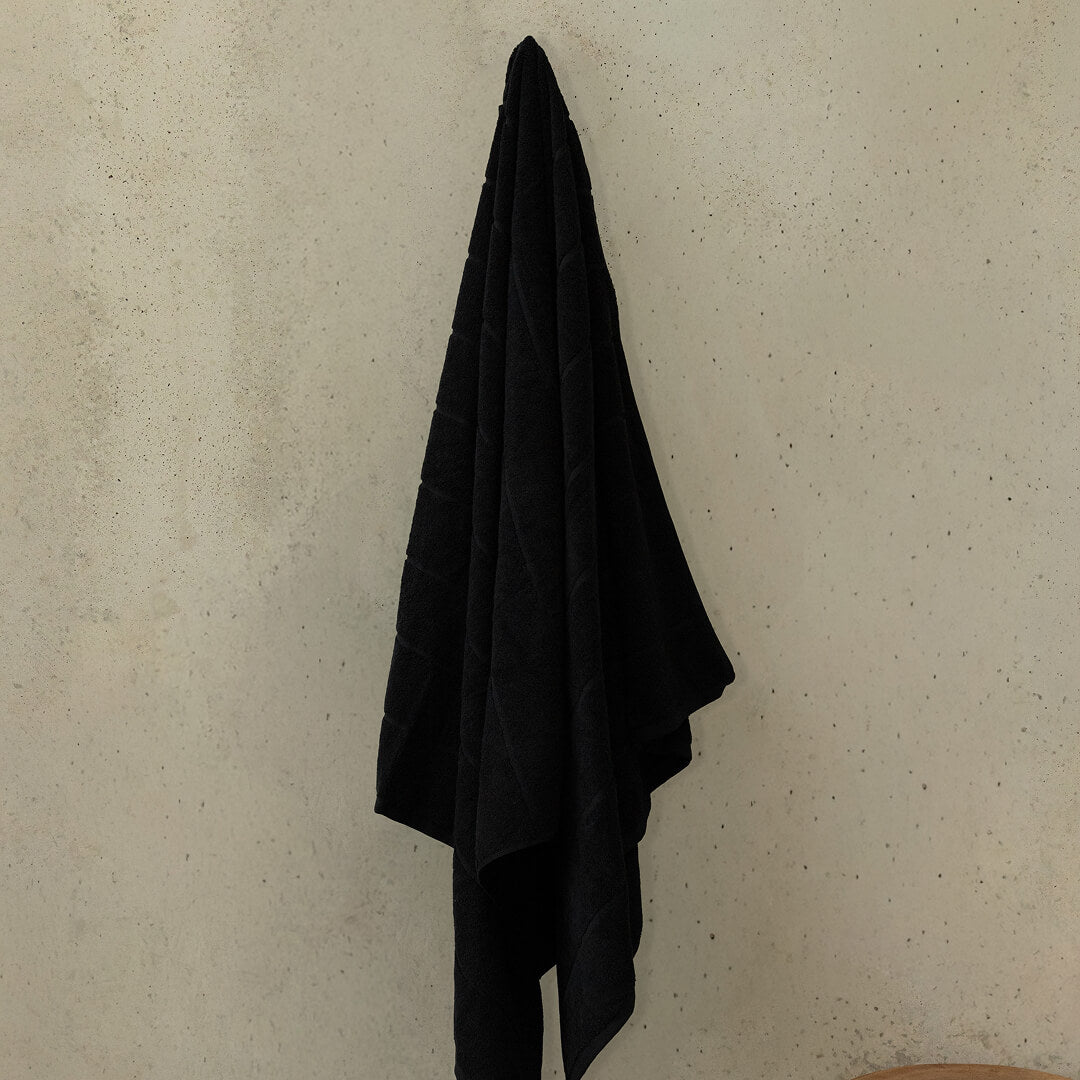 Black towel hanging on a hook against a beige wall.