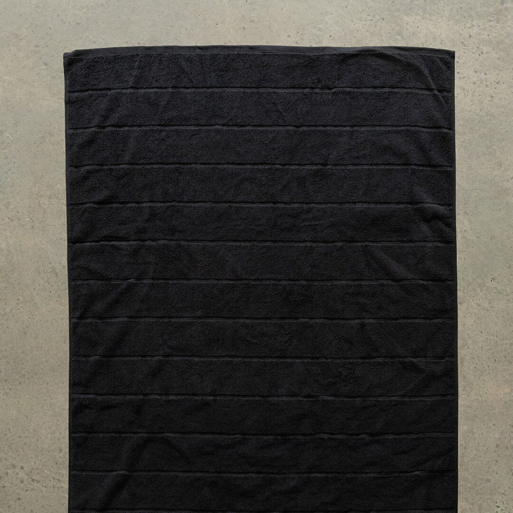 Black bath towel laid flat on a concrete floor.
