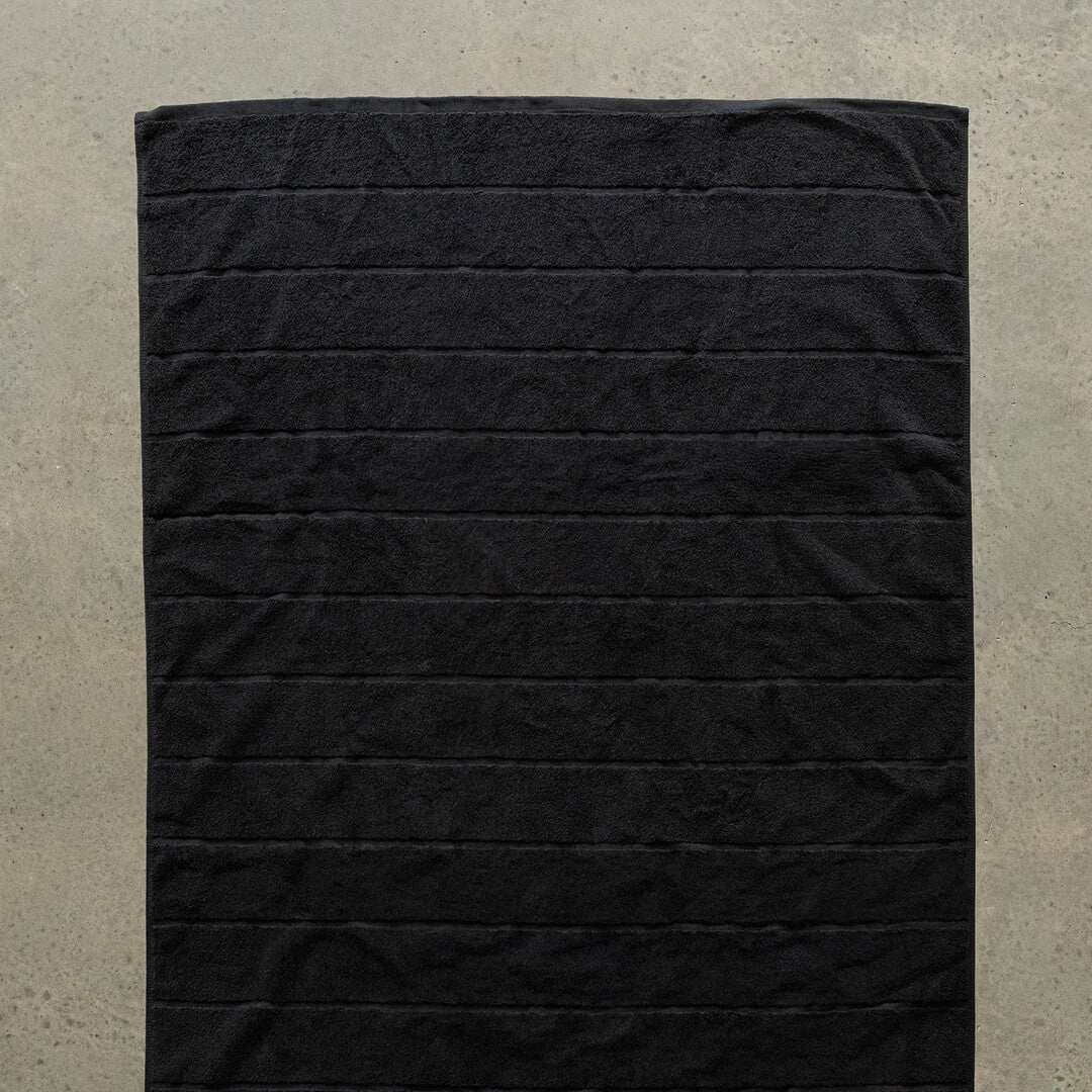 Black bath towel laid flat on a concrete floor.