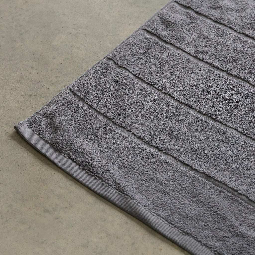 Charcoal grey bath towel on a concrete floor.