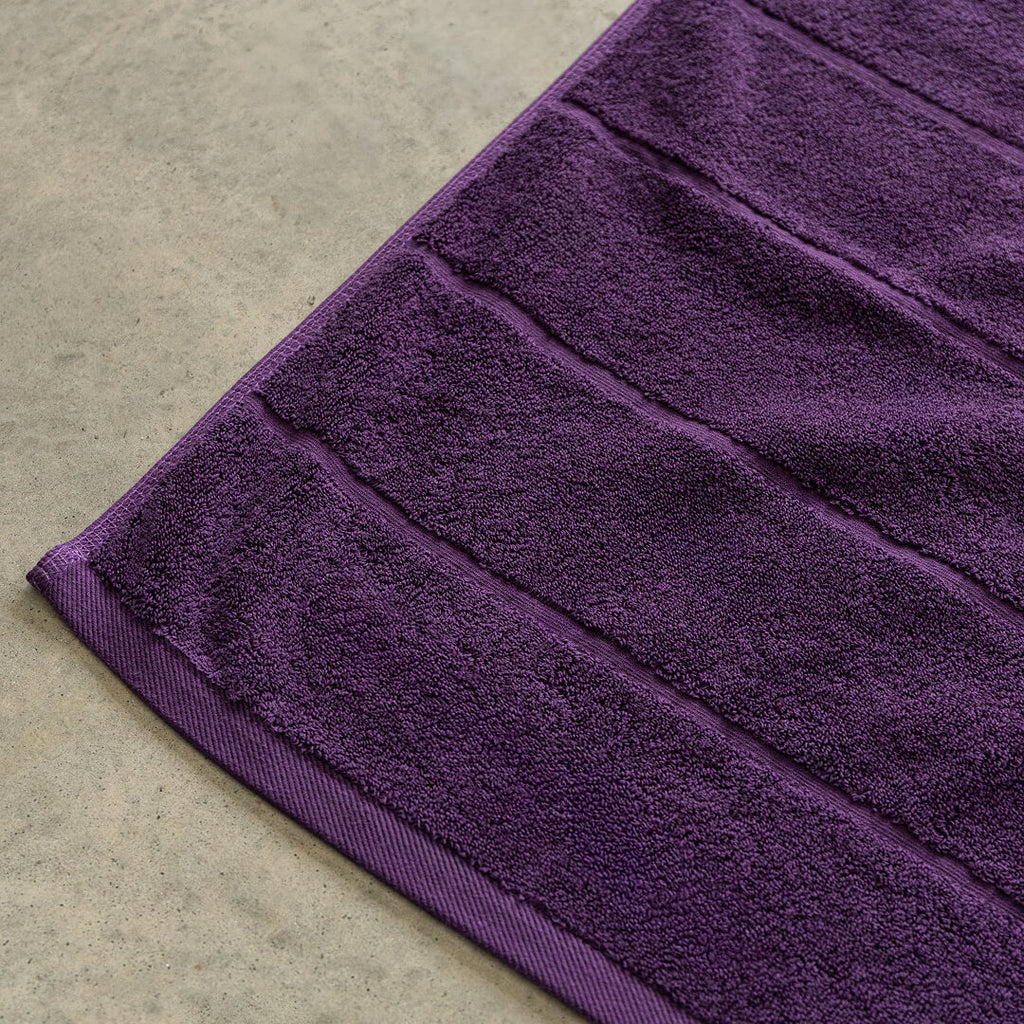 Close-up of a purple bath towel corner on a beige surface.