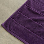 Close-up of a purple bath towel corner on a beige surface.