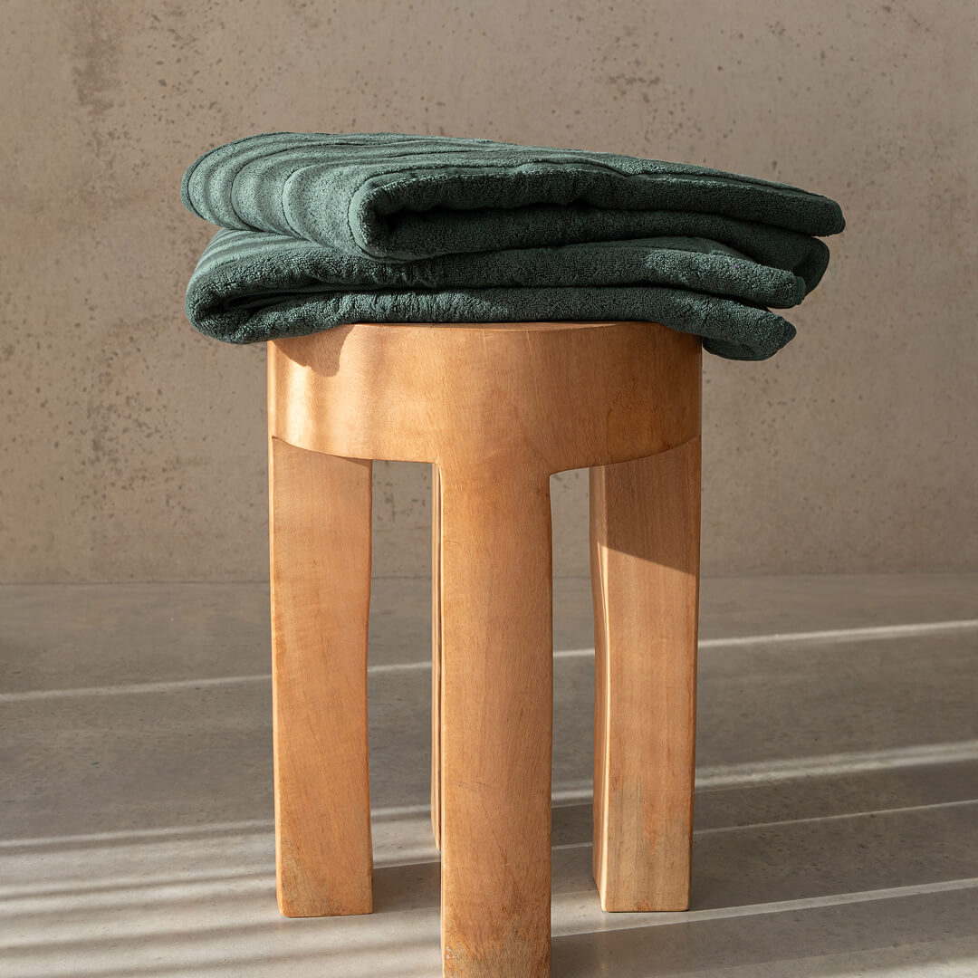 Wooden stool with green towels on top against a neutral background.