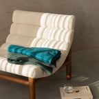 White cushioned chair with teal and green towel on a gray floor.