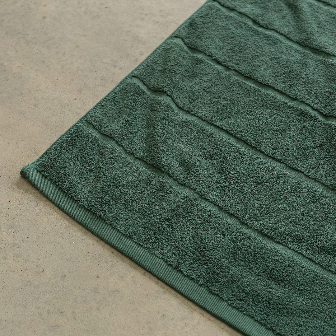 Green bath towel corner contrast against a beige floor.