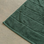 Green bath towel corner contrast against a beige floor.