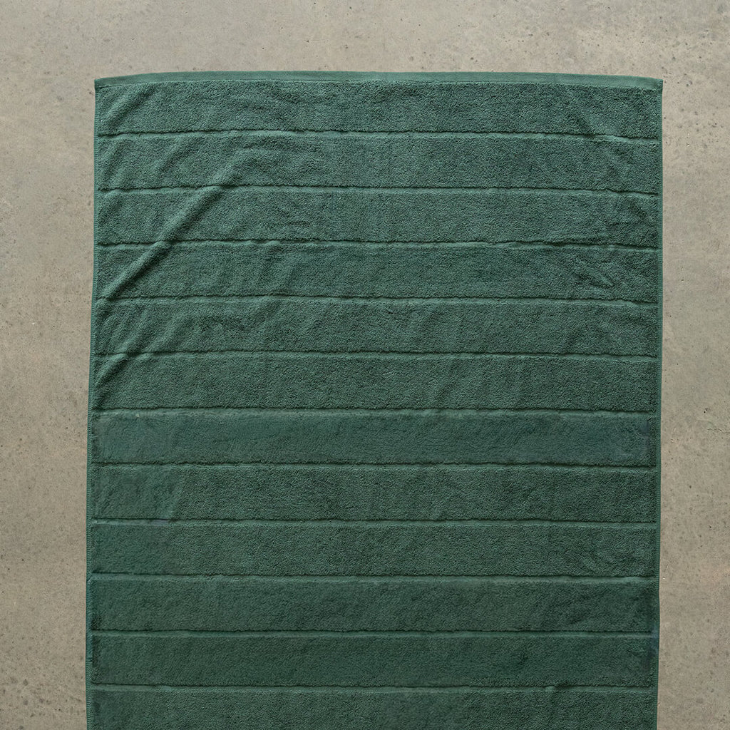 Green bath towel laid flat on a beige floor.