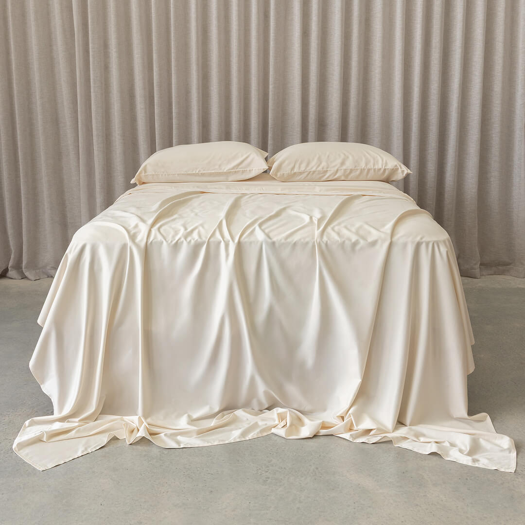 Cream bedspread and pillows on a bed with beige curtains in the background.