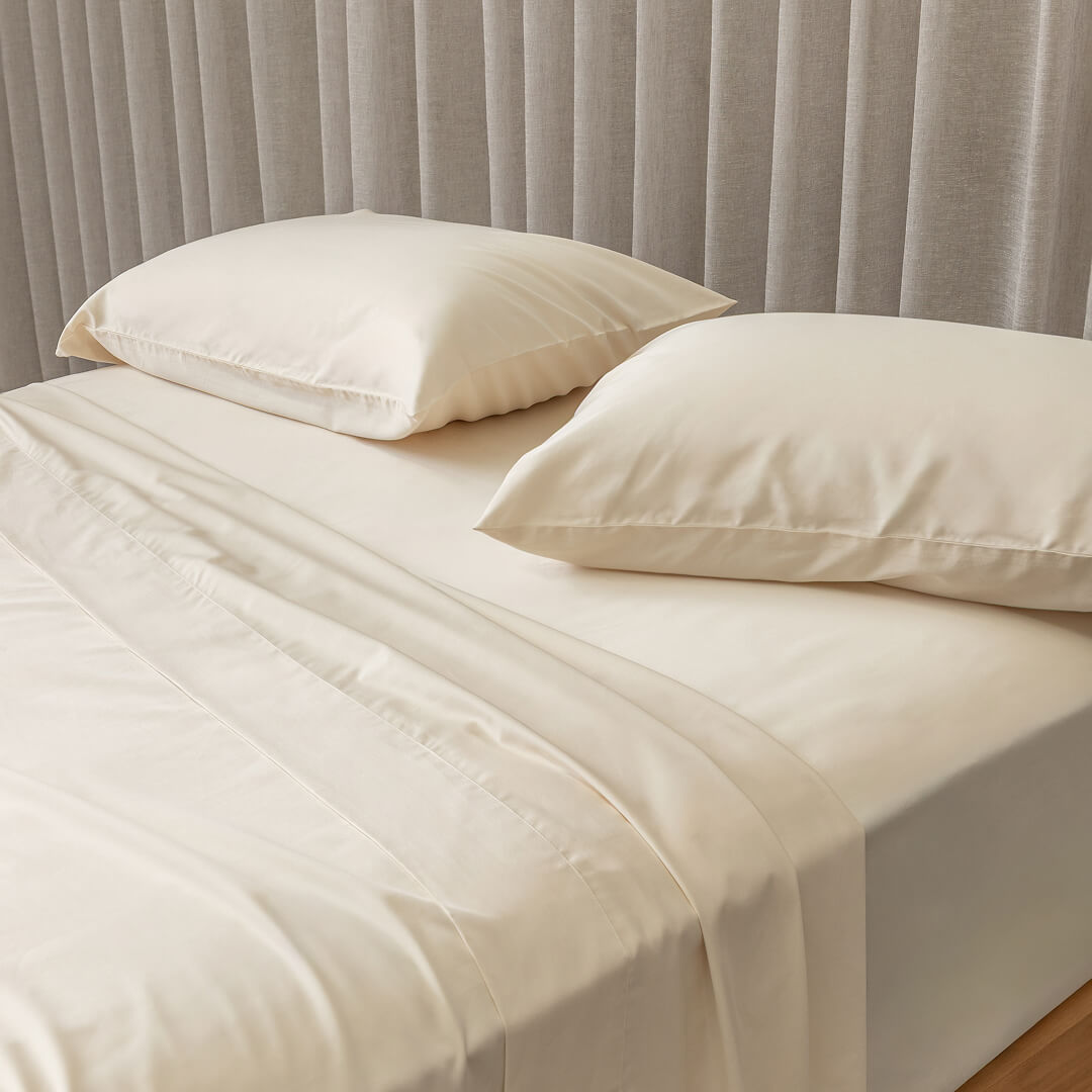Cream bed sheets and pillows on a bed with a neutral headboard.