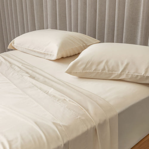 Cream bed sheets and pillows on a bed with a neutral headboard.
