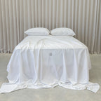 White bedspread with a brand logo on a bed against a neutral background