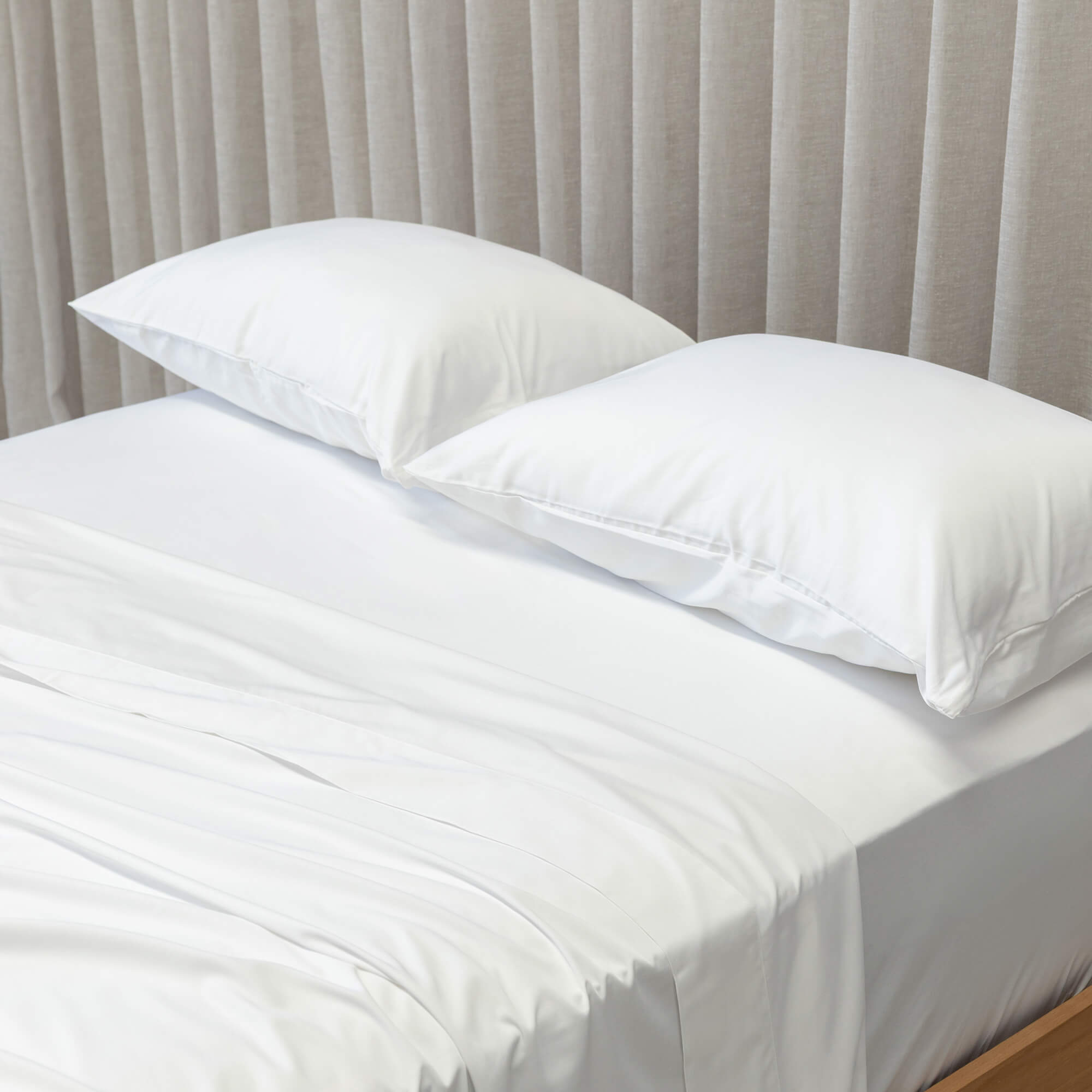 White bedspread on a bed with white pillows against a beige curtain background