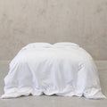 White comforter on a bed against a plain wall.