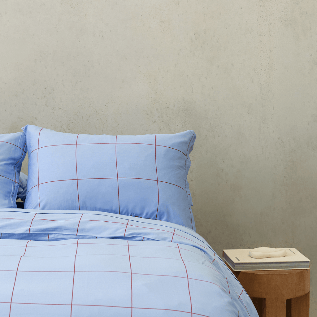 Front view of light blue grid-patterned quilt cover set next to a wooden side table