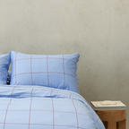 Front view of light blue grid-patterned quilt cover set next to a wooden side table