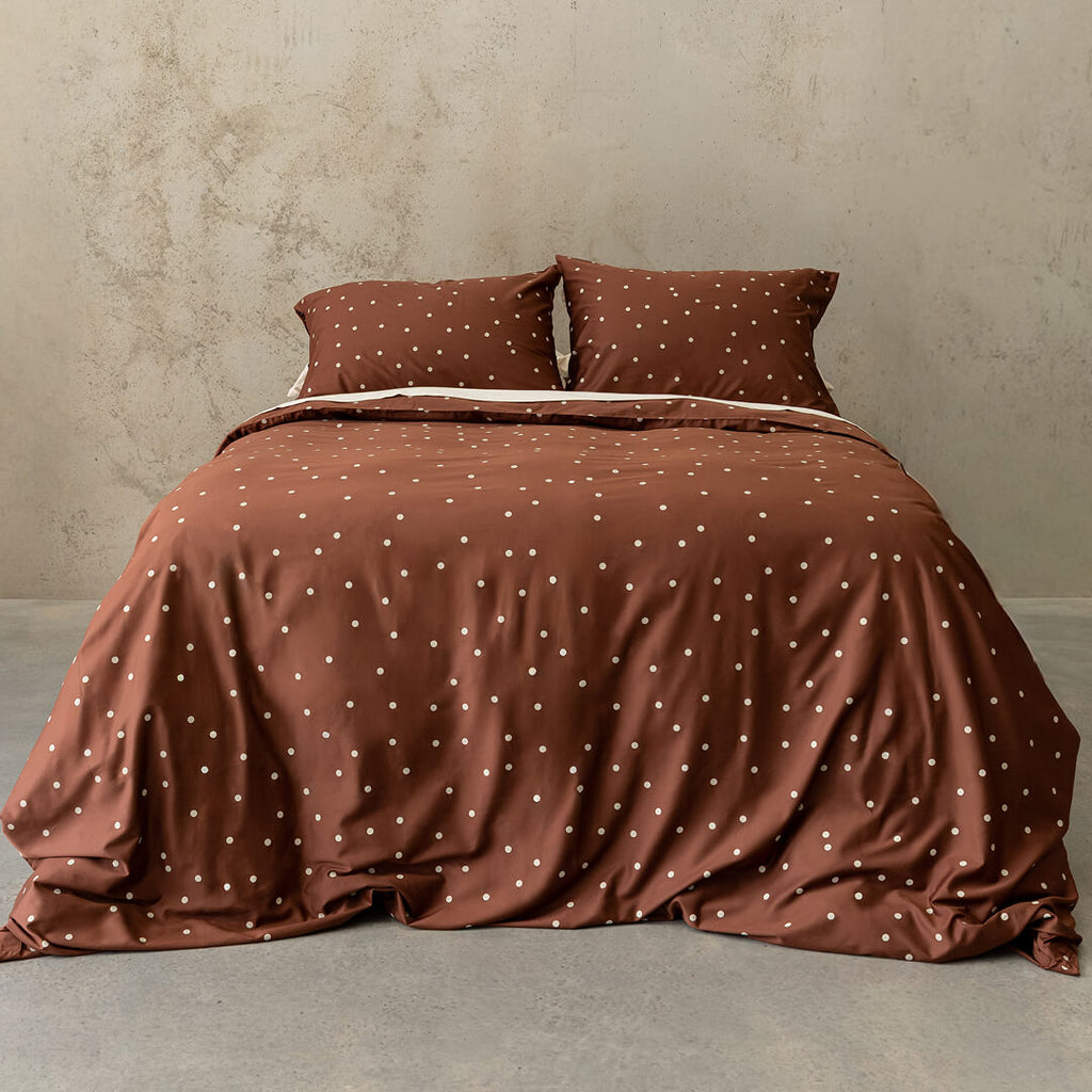 Brown polka dot bedding set on a bed against a beige wall.