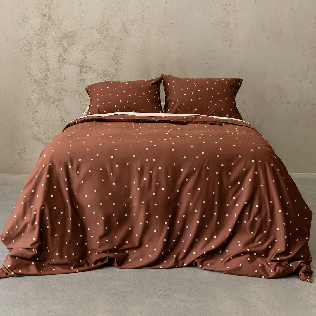 Brown polka dot bedding set on a bed against a beige wall.