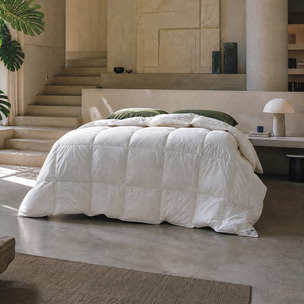 White comforter on a bed in a modern bedroom with concrete floor and stone walls.