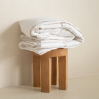 Stack of white folded blankets on a wooden stool against a beige wall.