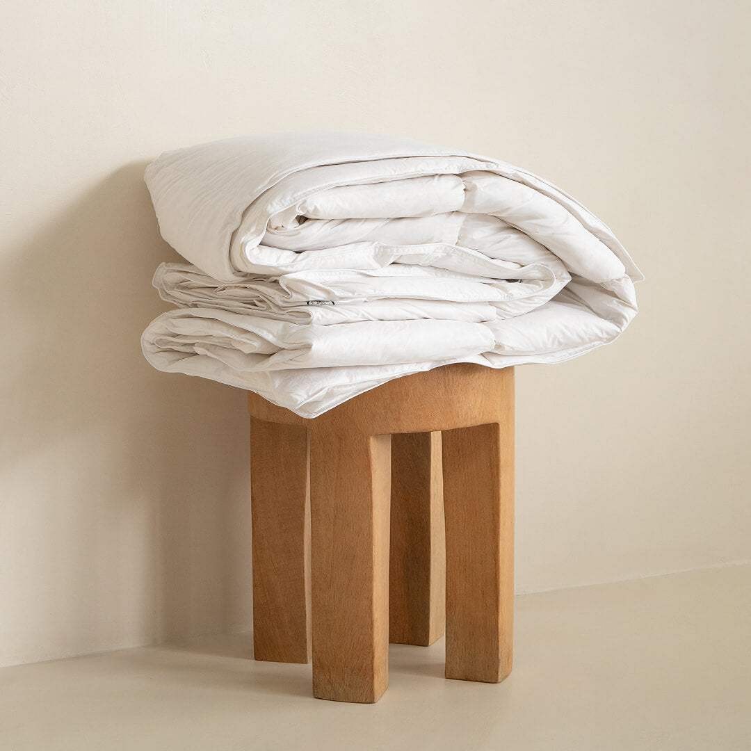 Stack of white folded blankets on a wooden stool against a beige wall.