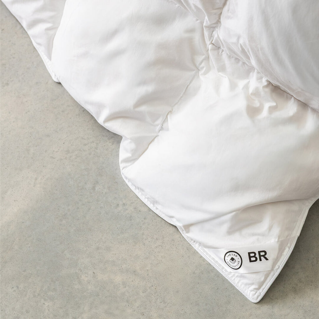 White comforter with a brand logo on a light grey surface.