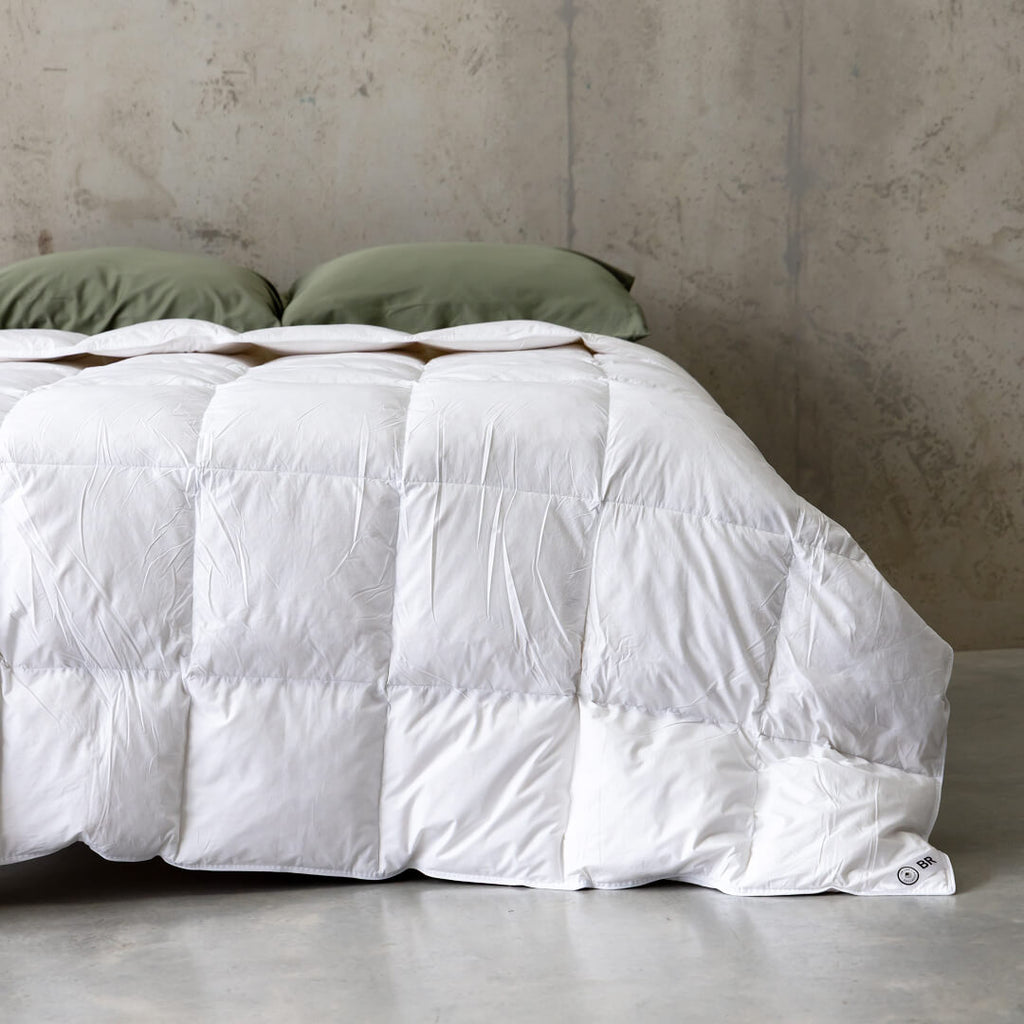 White winter quilt insert on a bed with green pillows against a textured wall.