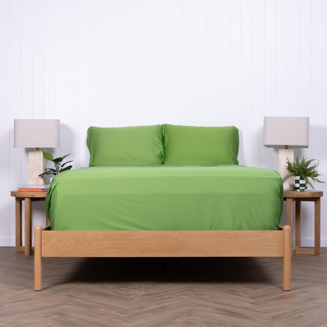Minimalist shot of green TLC bedding neatly tucked into wooden bed frame.