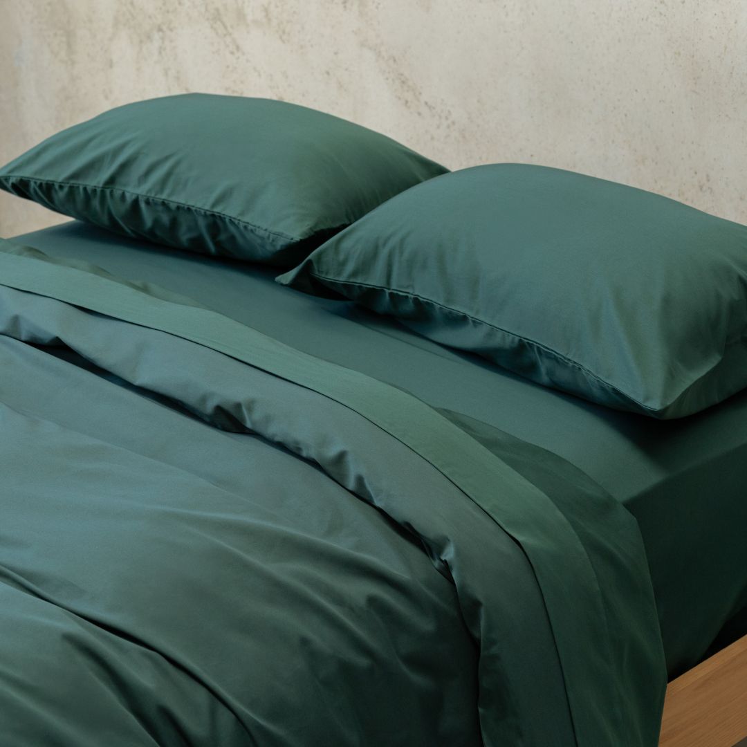 Green bedding set with two pillows on a bed against a neutral wall.