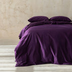 Purple bedding set on a bed against a beige wall.