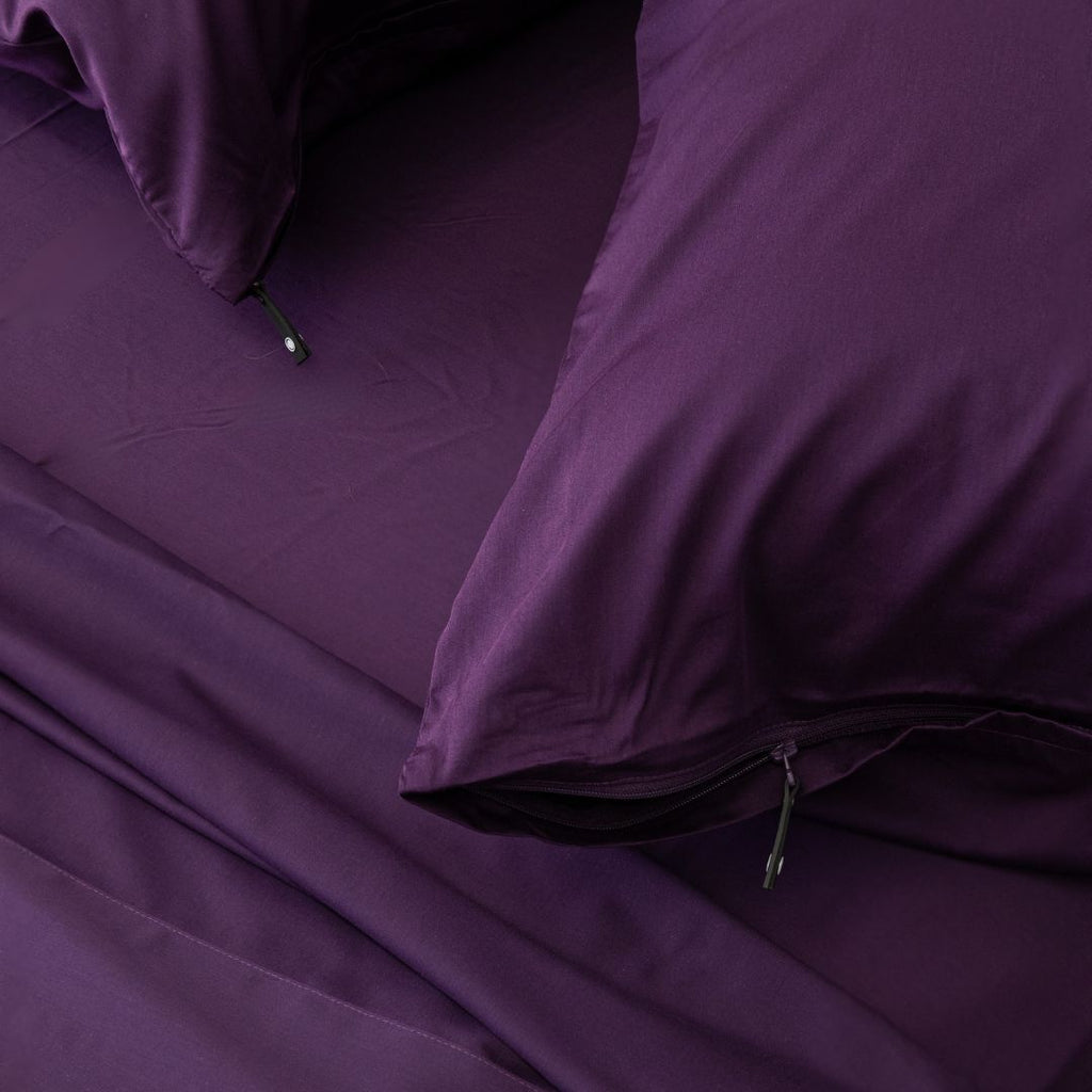 Purple bedding set with pillows and a fitted sheet on a bed.