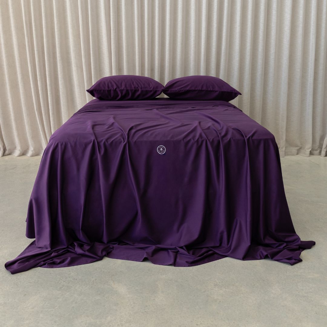 Purple bedspread on a bed with pillows against a neutral background
