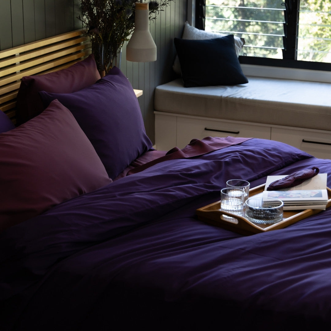 Bedroom with purple bedding and pillows, a tray with items on a windowsill.