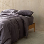 Gray bedding set on a bed with a wooden headboard against a beige wall.