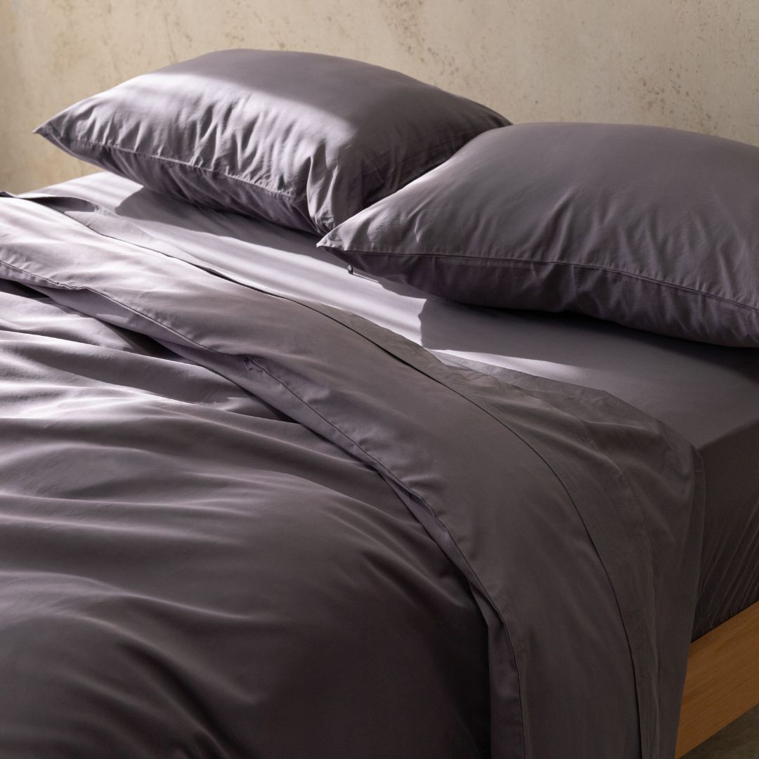 Gray bedding set with two pillows on a bed against a neutral wall.