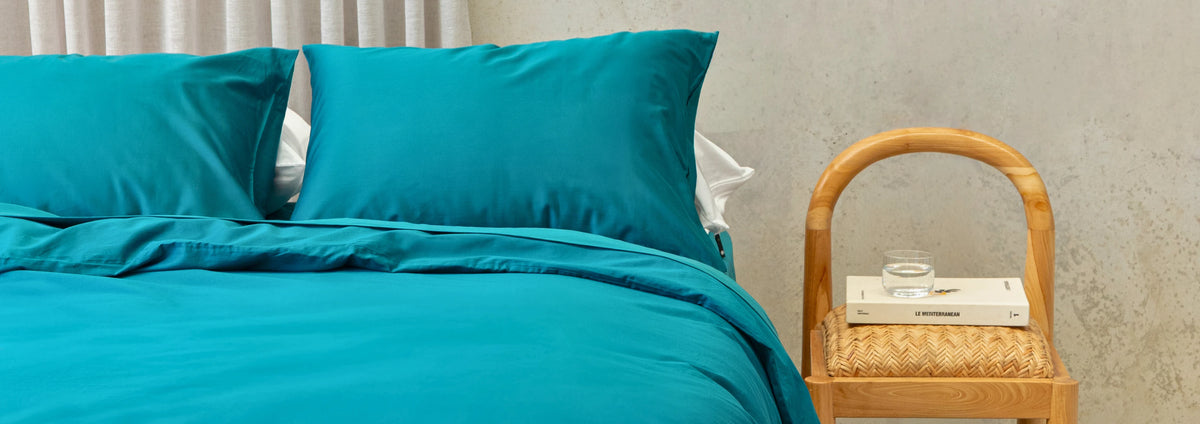 Teal bedding set on a bed with a wooden nightstand in the background