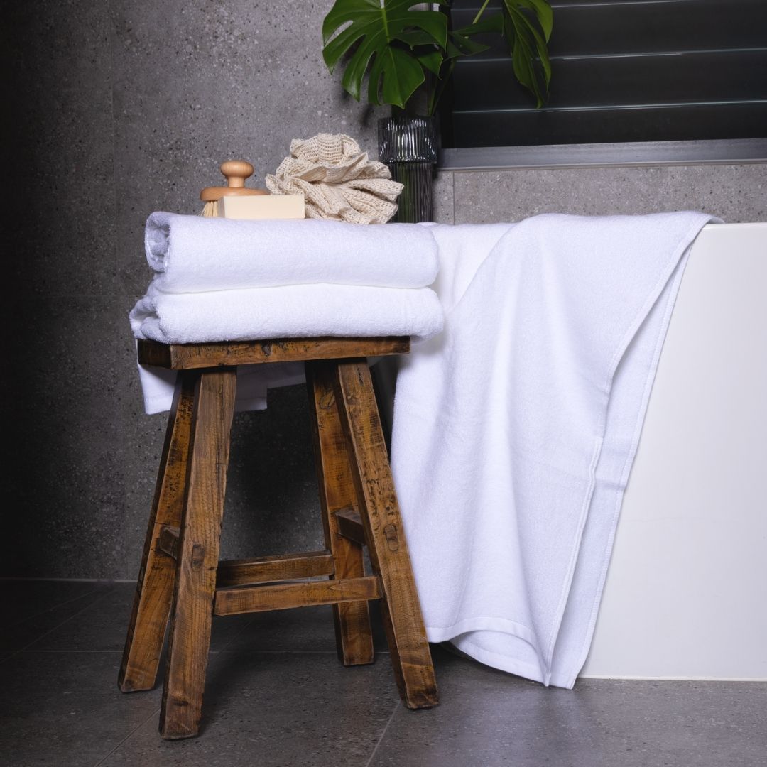 White bath towels styled in a bathroom, next to a bath tub.