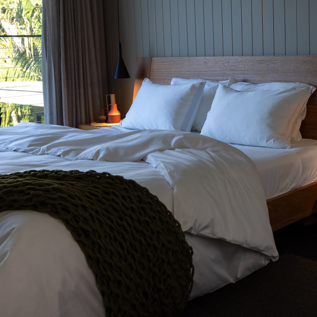 Bedroom with a neatly made bed featuring white pillows and duvet, and a dark green throw blanket.