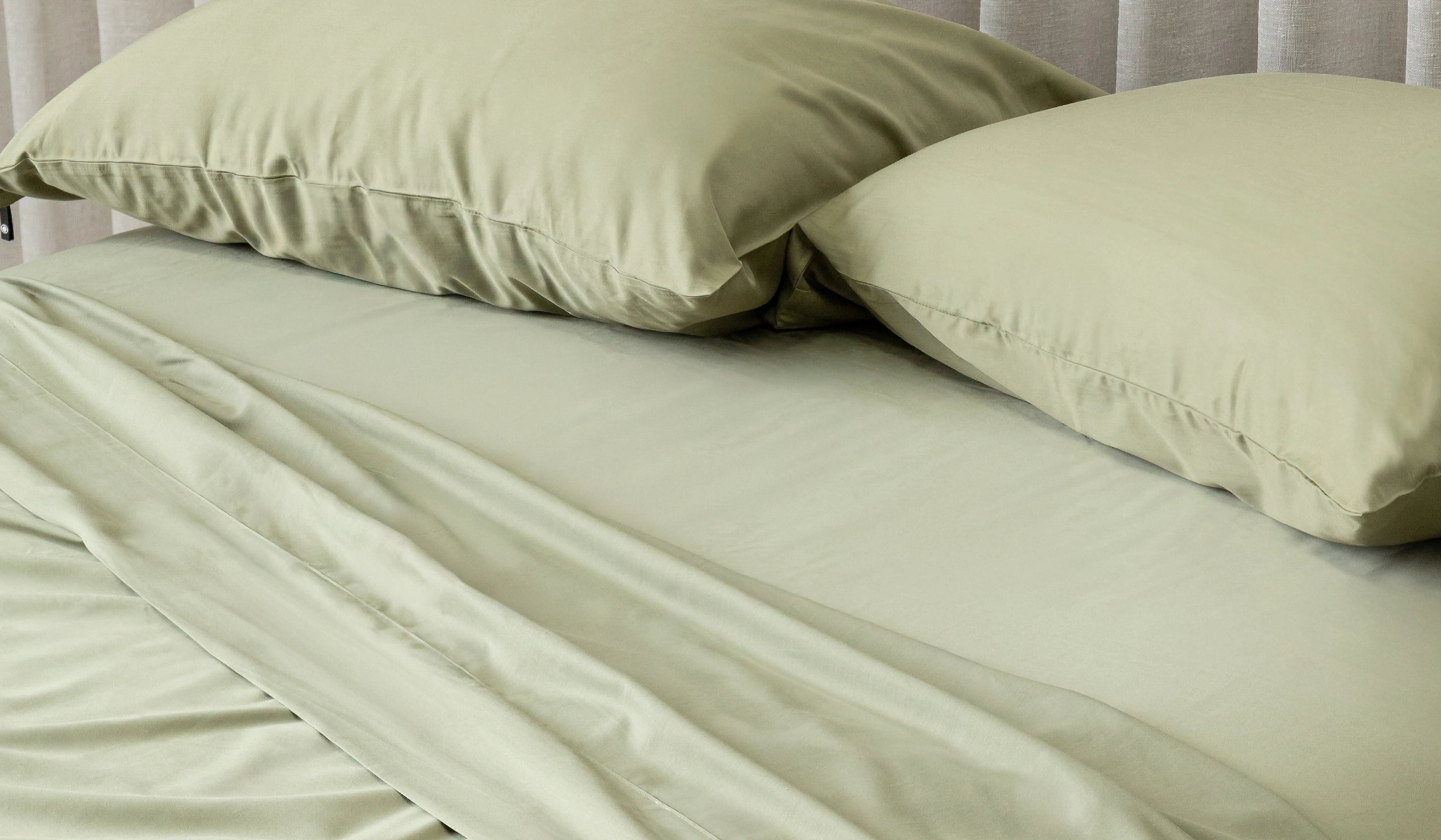 Green bed sheets and pillows on a bed with a neutral background