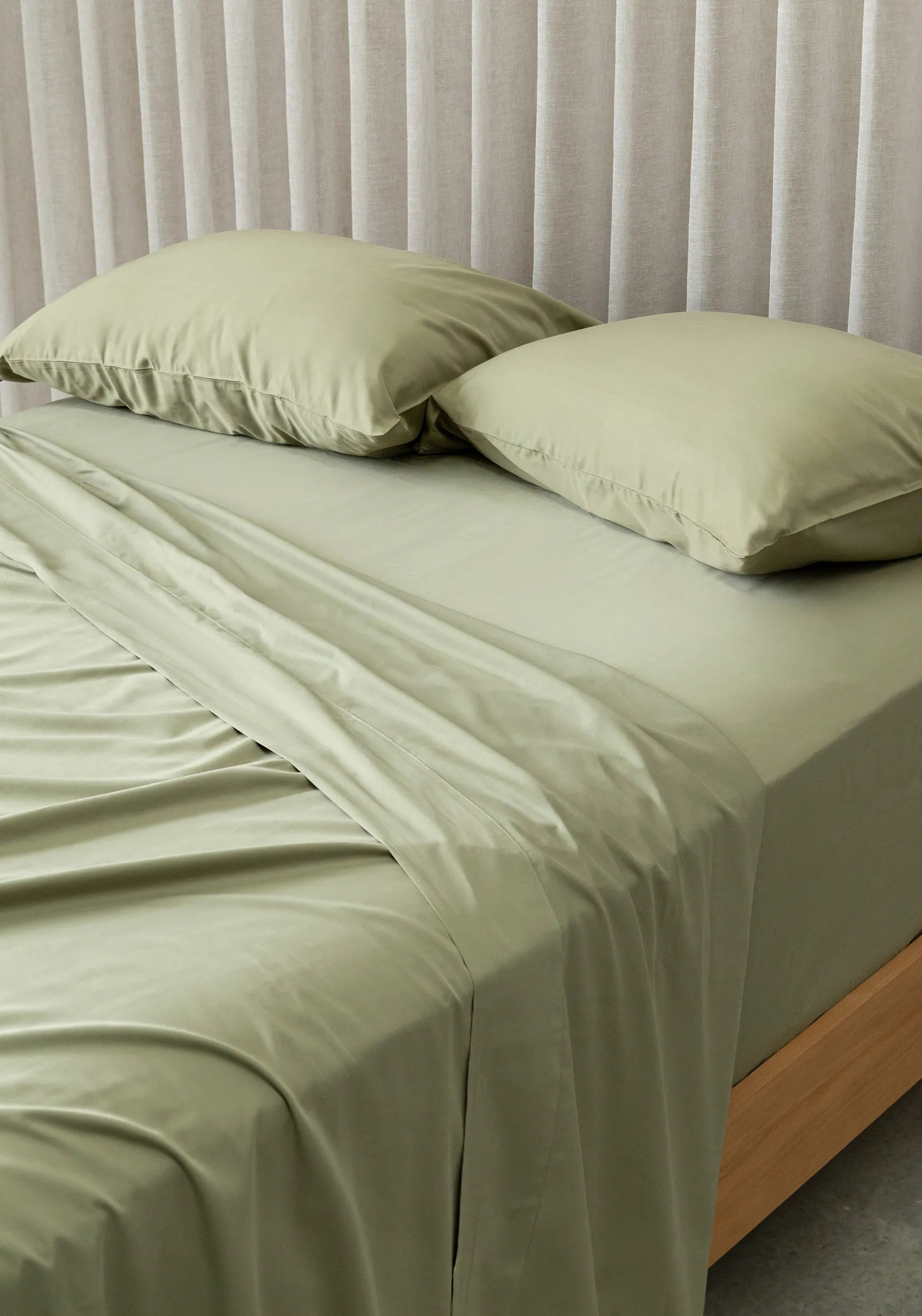 Bed with green bedding and pillows against a neutral headboard.