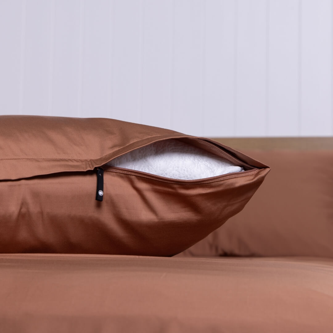 Close-up of a rust-coloured pillowcase partially unzipped to reveal a white pillow insert.