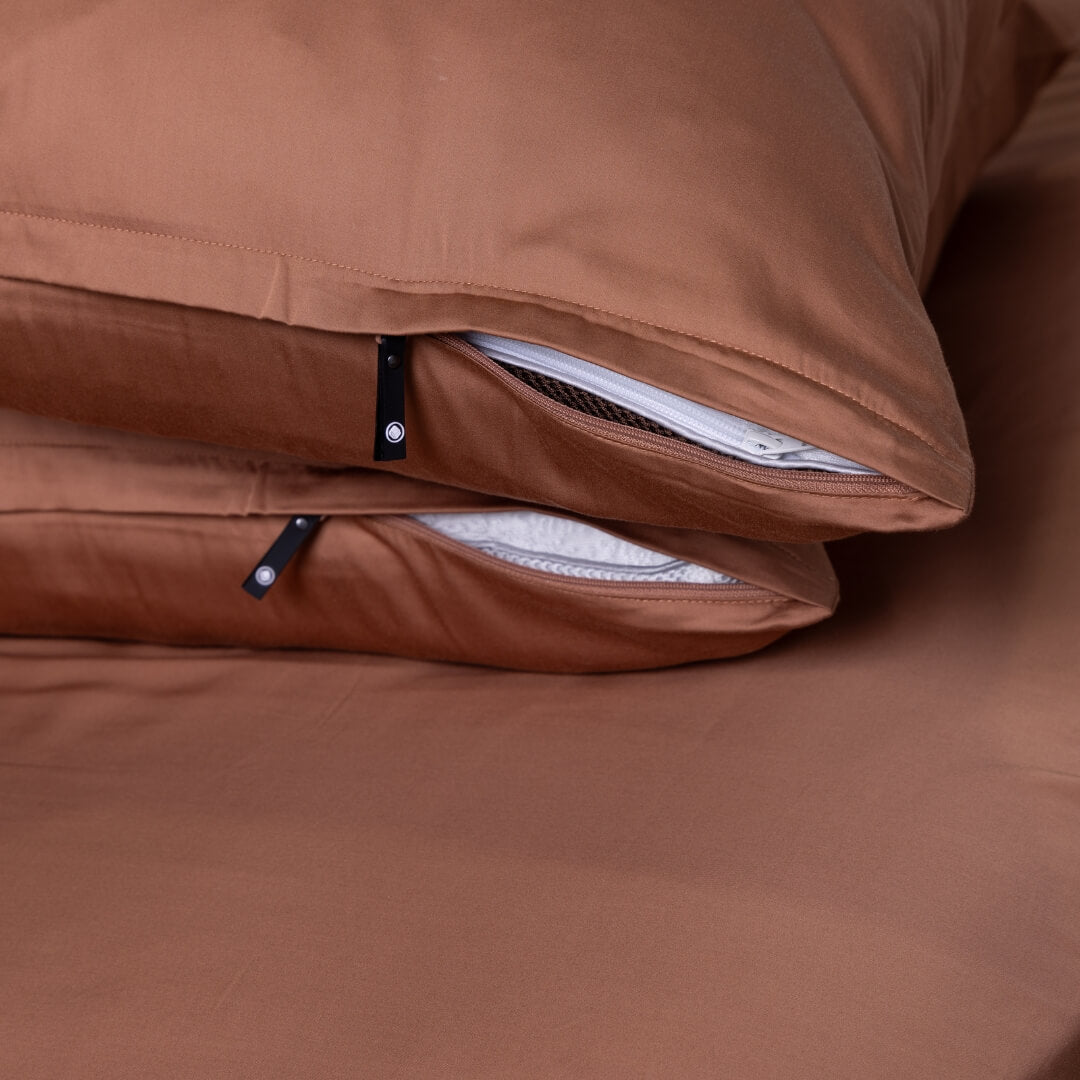 Two stacked rust-coloured zippered pillowcases with pillows inside from The Lad Collective.