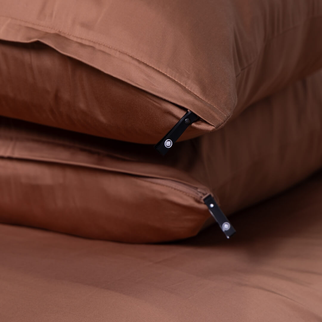 Close-up of rust-coloured pillowcases with black zips from The Lad Collective’s bedding set.