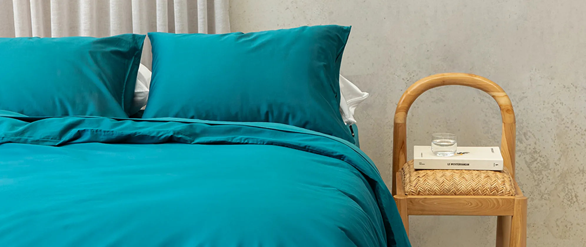 Teal bedding set on a bed with a wooden side table in the background