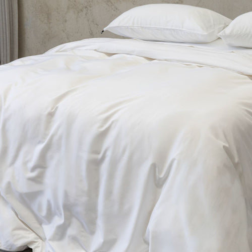 White quilt on a bed with pillows against a neutral wall.